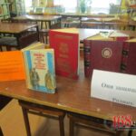 Книжная выставка в библиотеке: книги на столах и стеллажи на заднем плане