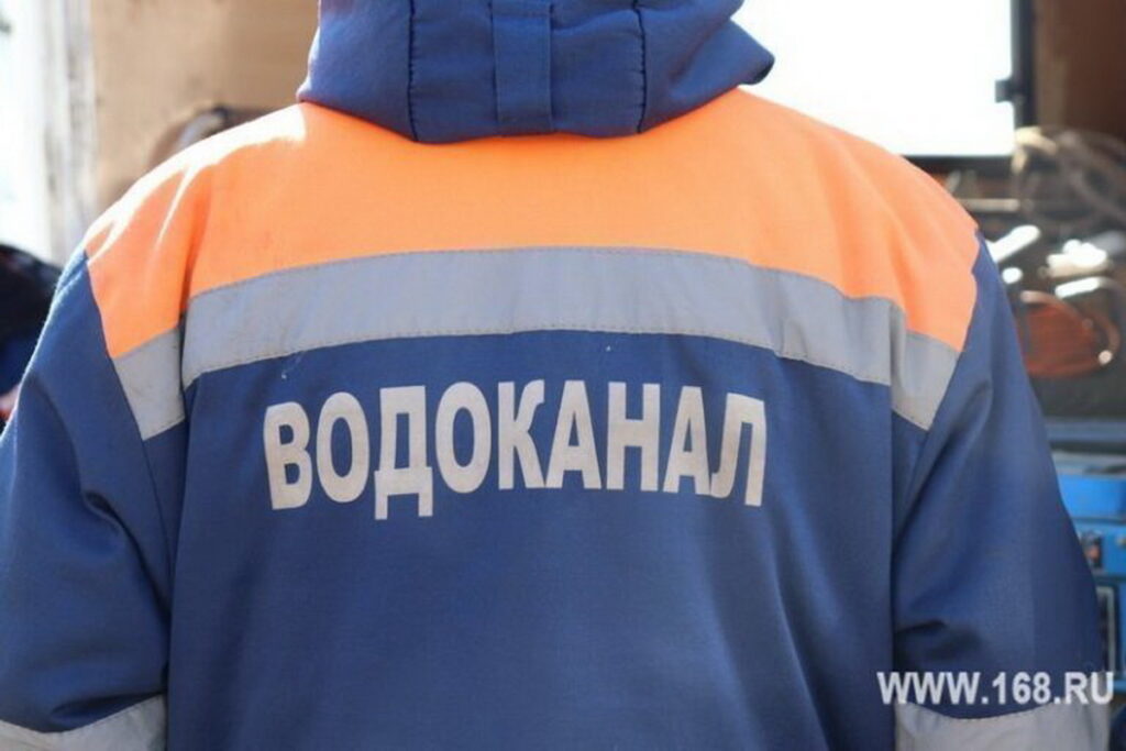 Работник со спины в сине-оранжевой спецодежде со светоотражающими полосами и надписью «Водоканал»