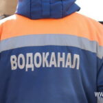 Работник со спины в сине-оранжевой спецодежде со светоотражающими полосами и надписью «Водоканал»