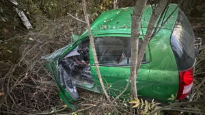Сильно поврежденный зеленый автомобиль среди деревьев и кустарника