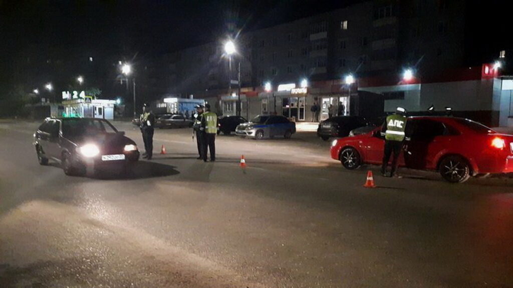 Сотрудники ДПС проверяют автомобили на ночной дороге, огражденной сигнальными конусами