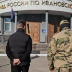 Мужчина со скованными за спиной руками и человек в камуфляже идут к входу в здание управления МВД