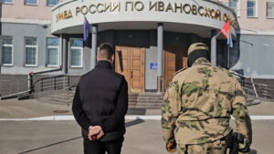 Мужчина со скованными за спиной руками и человек в камуфляже идут к входу в здание управления МВД