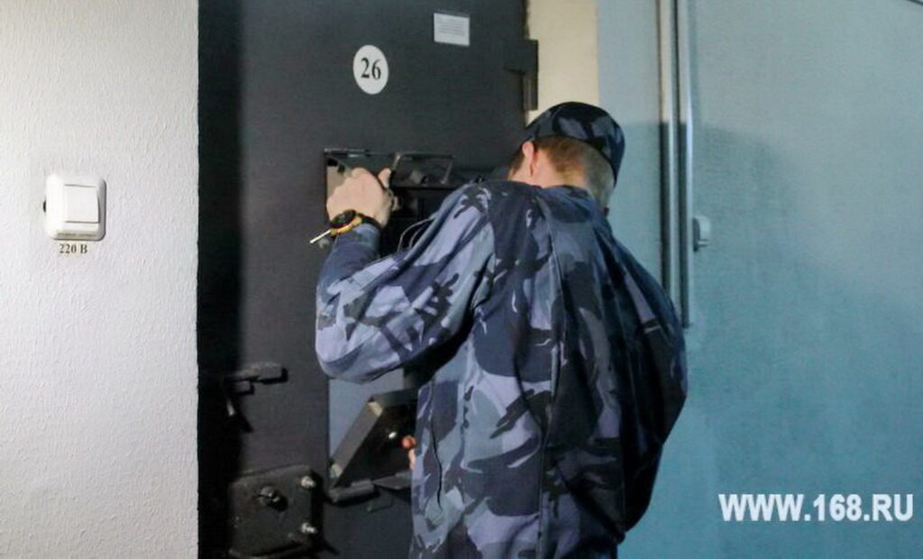 Сотрудник в камуфляжной форме открывает металлическую дверь с номером 26