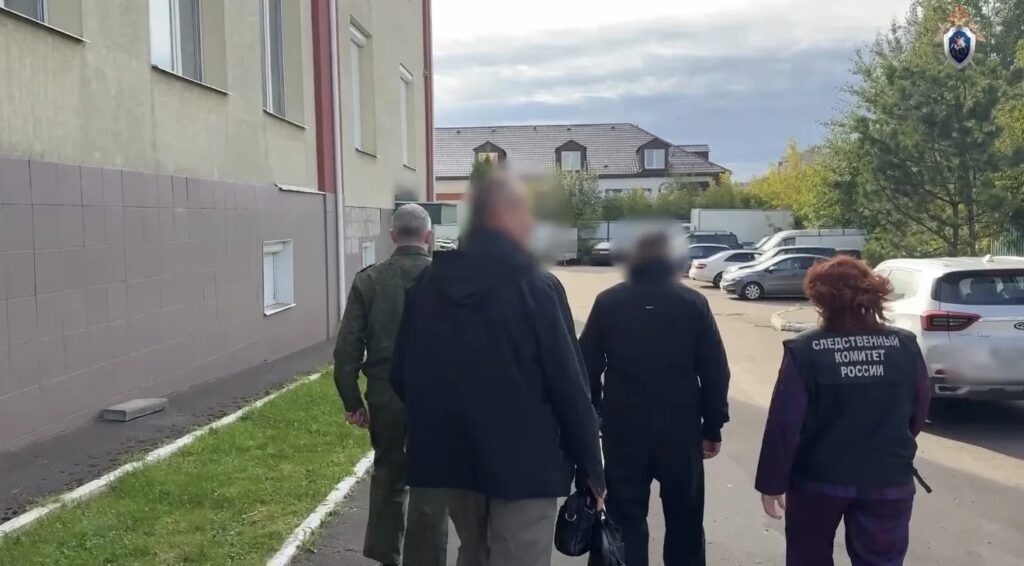 Четверо людей идут вдоль здания мимо припаркованных машин, на жилете женщины надпись «Следственный комитет России»