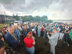 Большая группа людей собралась у припаркованных автомобилей на берегу водоёма
