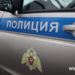 Крупный план мокрой от дождя двери служебного автомобиля с синей полосой, надписью «Полиция» и эмблемой
