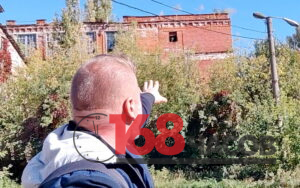 Мужчина со спины указывает рукой на заросшее краснокирпичное промышленное здание с разбитыми окнами