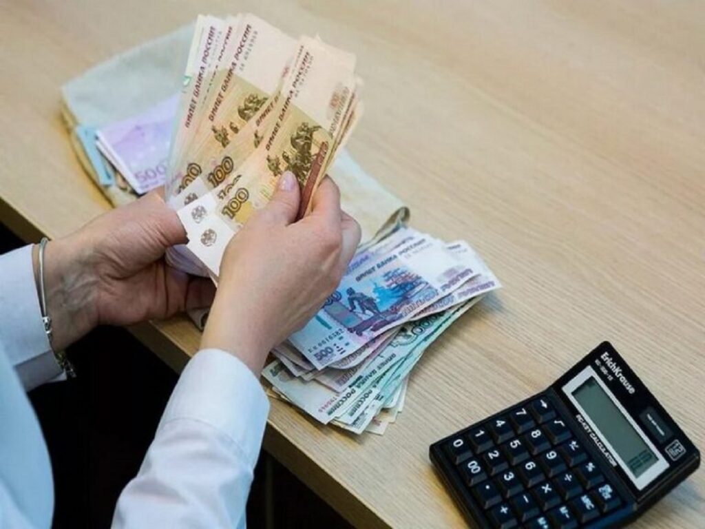 Человек пересчитывает российские банкноты за столом, рядом лежат пачки денег и калькулятор