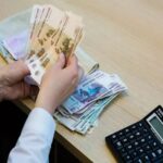 Человек пересчитывает российские банкноты за столом, рядом лежат пачки денег и калькулятор