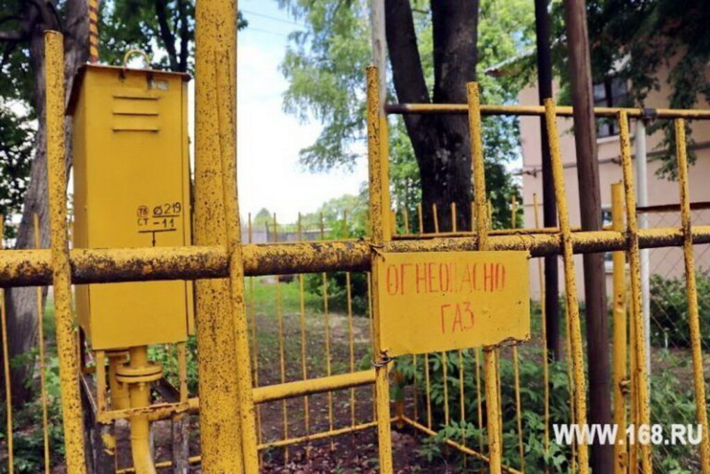 Жёлтый газовый шкаф и трубы за металлическим ограждением с табличкой «Огнеопасно. Газ»