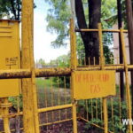 Жёлтый газовый шкаф и трубы за металлическим ограждением с табличкой «Огнеопасно. Газ»