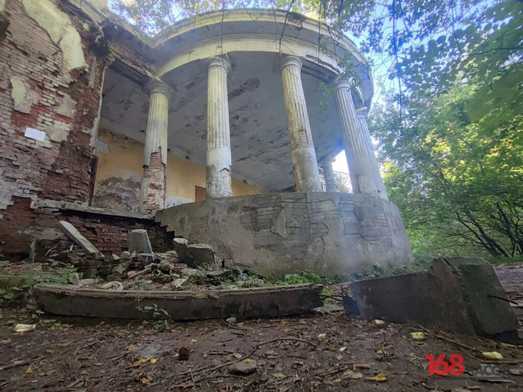 Полуразрушенная кирпичная терраса с высокими колоннами и осыпавшейся штукатуркой среди деревьев