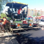 Рабочие укладывают асфальт с помощью асфальтоукладчика на городской улице рядом с проезжающими автомобилями