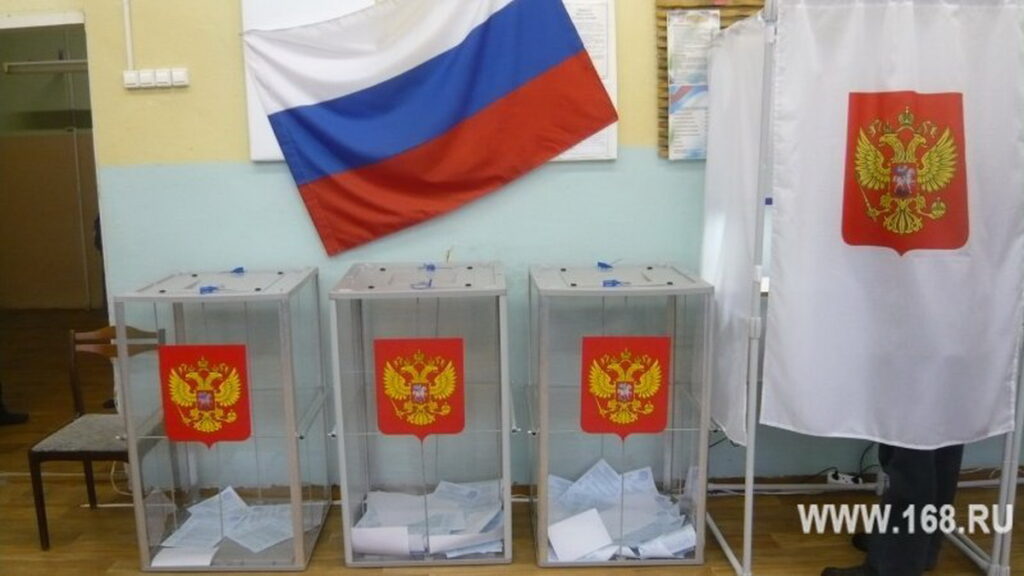Три прозрачные урны с бюллетенями и закрытая кабина для голосования на фоне российского флага
