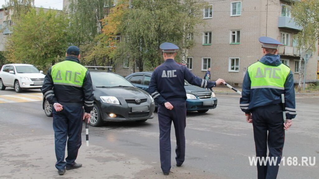 Три сотрудника ДПС с жезлами регулируют движение автомобилей на перекрёстке у жилого дома