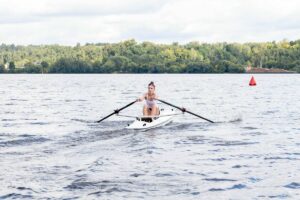 Спортсменка гребёт на одиночной лодке по реке возле красного буя