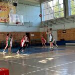 Юные баскетболистки в красно-белой и зелёно-белой форме играют у кольца в спортивном зале