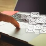 рука нажимает на тачпад ноутбука; поверх кадра наложены значки конвертов (электронные сообщения)