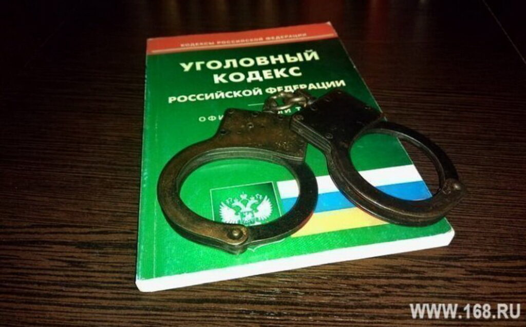 Металлические наручники лежат на книге «Уголовный кодекс Российской Федерации» на деревянном столе