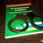 Металлические наручники лежат на книге «Уголовный кодекс Российской Федерации» на деревянном столе