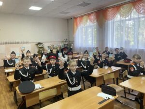 Школьники в кадетской форме стоят за партами и показывают небольшие сувениры в упаковках