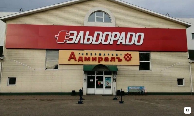 Фасад торгового центра с большой красной вывеской «Эльдорадо» и жёлтой вывеской «Адмиралъ» над входом.
