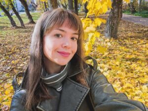 Молодая женщина делает селфи в осеннем парке среди деревьев с жёлтой листвой