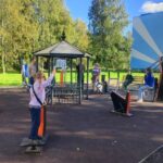 Дети и взрослые занимаются на уличных тренажёрах вокруг беседки во дворе жилого дома