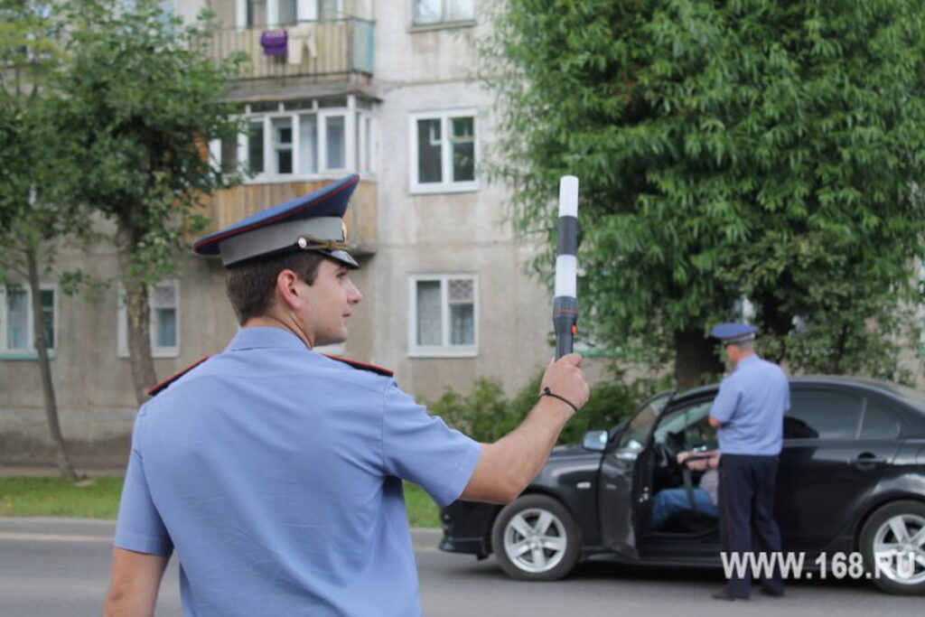 Сотрудник автоинспекции с жезлом останавливает транспорт, пока его коллега беседует с водителем у черного автомобиля