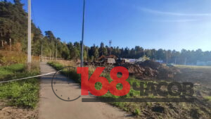 Перекрытая лентой дорожка проходит вдоль площадки с экскаватором, самосвалом и кучами грунта