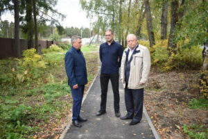 Трое мужчин стоят на узком асфальтированном тротуаре среди деревьев