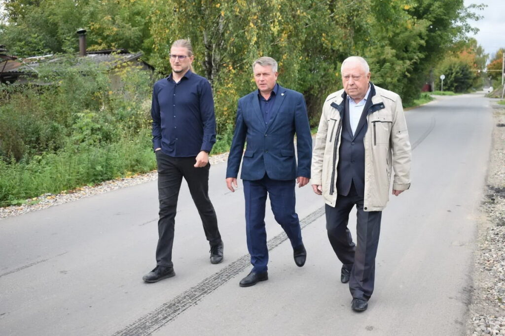 Трое мужчин идут по новой асфальтированной дороге вдоль деревьев и частных домов