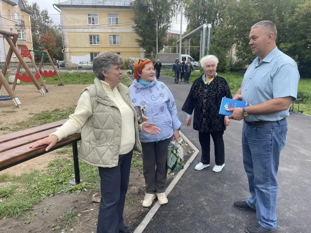 Три пожилые женщины беседуют с мужчиной на новой асфальтированной аллее рядом с детской площадкой