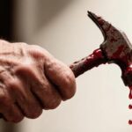 Пожилая рука сжимает молоток, покрытый красной жидкостью, с бойка падают капли