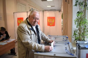 Пожилой мужчина опускает бюллетень в урну для голосования на избирательном участке.