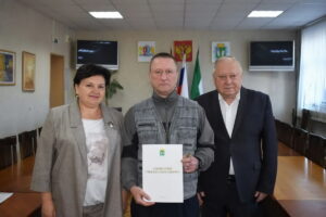 Две женщины и мужчина позируют в зале, держа папку с документами и ключи