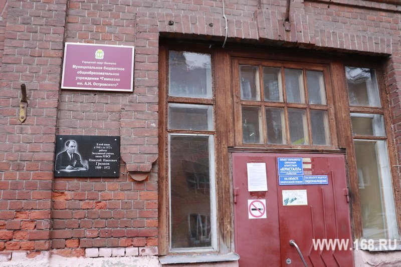 Вход в кирпичное кирпичное здание гимназии: дверной проём, табличка с названием учреждения и мемориальная доска.