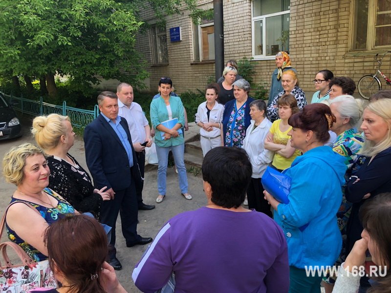 группа жильцов и чиновник во дворе кирпичного многоквартирного дома