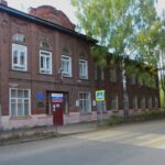 Двухэтажное кирпичное здание гимназии у дороги с пешеходным переходом и берёзами