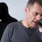 мужчина разговаривает по мобильному; на заднем плане человек в тёмной маске/балаклаве тоже с телефоном