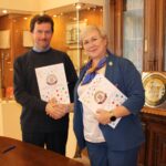 Мужчина и женщина пожимают руки и держат папки с документами в кабинете с книжными шкафами и витринами.