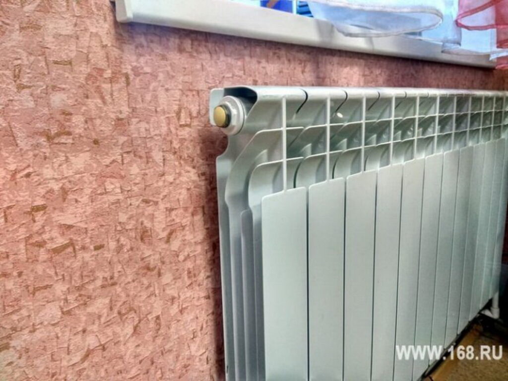 Белый секционный радиатор отопления установлен под подоконником у стены с розовой отделкой