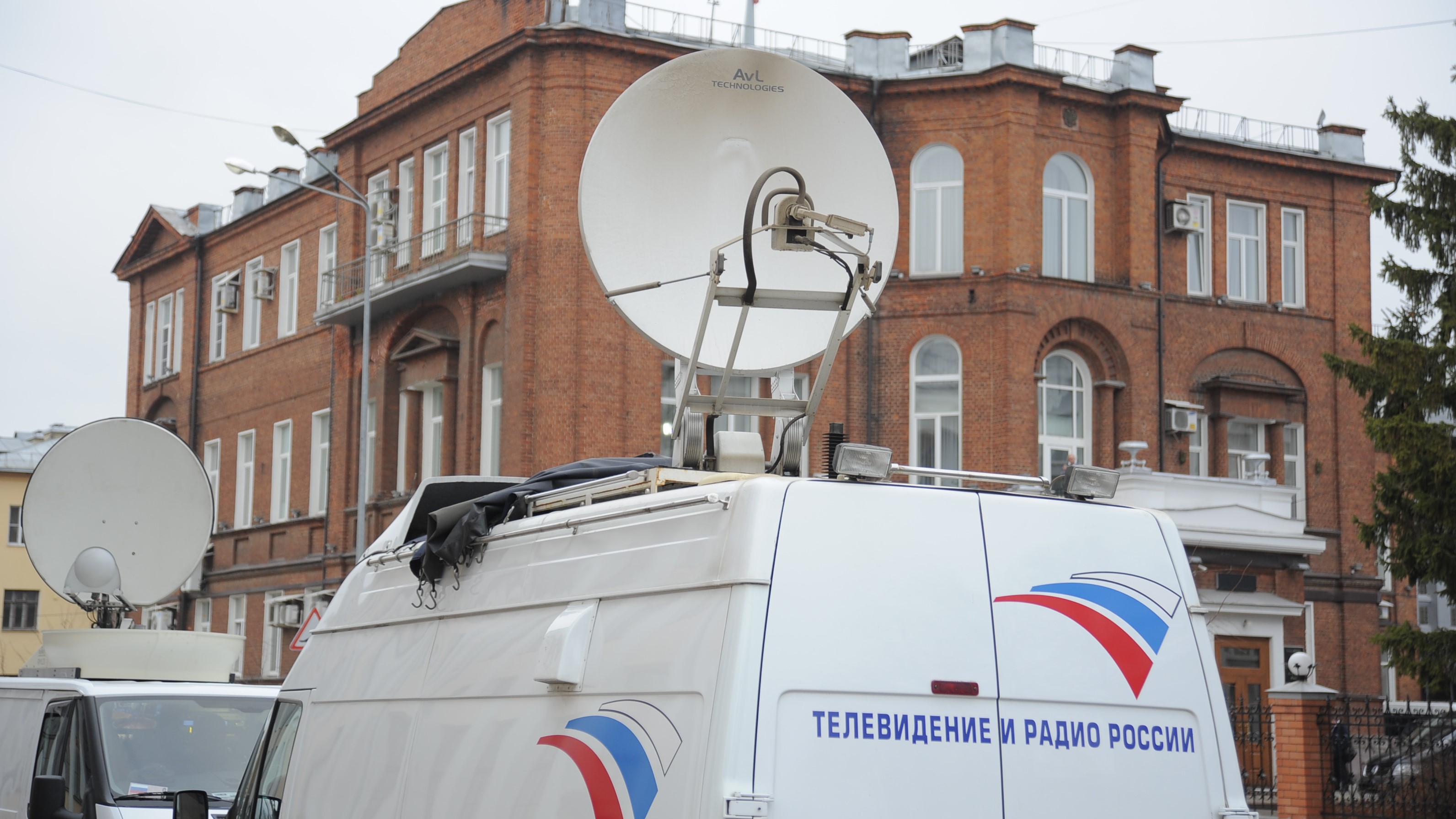 Репортажный автомобиль со спутниковой антенной и надписью «Телевидение и радио России» на фоне кирпичного здания.