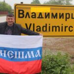 Мужчина держит российский флаг с надписью «Кинешма» возле жёлтого указателя «Владимирци».