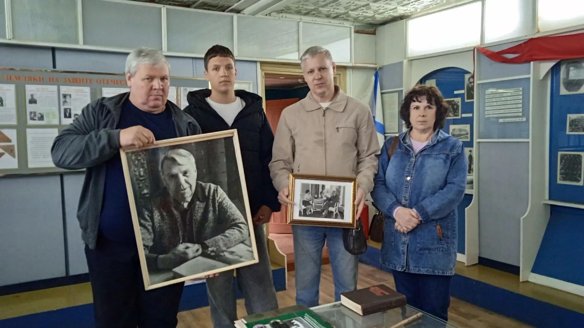 Четверо человек в музейном интерьере держат в руках две рамки с чёрно‑белыми фотографиями (одна большая портретная), на стенах — музейные стенды и экспонаты.
