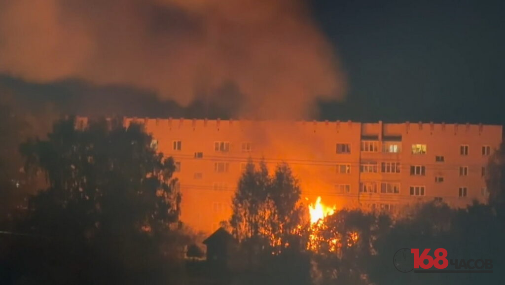 Ночью за деревьями видны яркое пламя и густой дым на фоне освещённого заревом многоэтажного дома