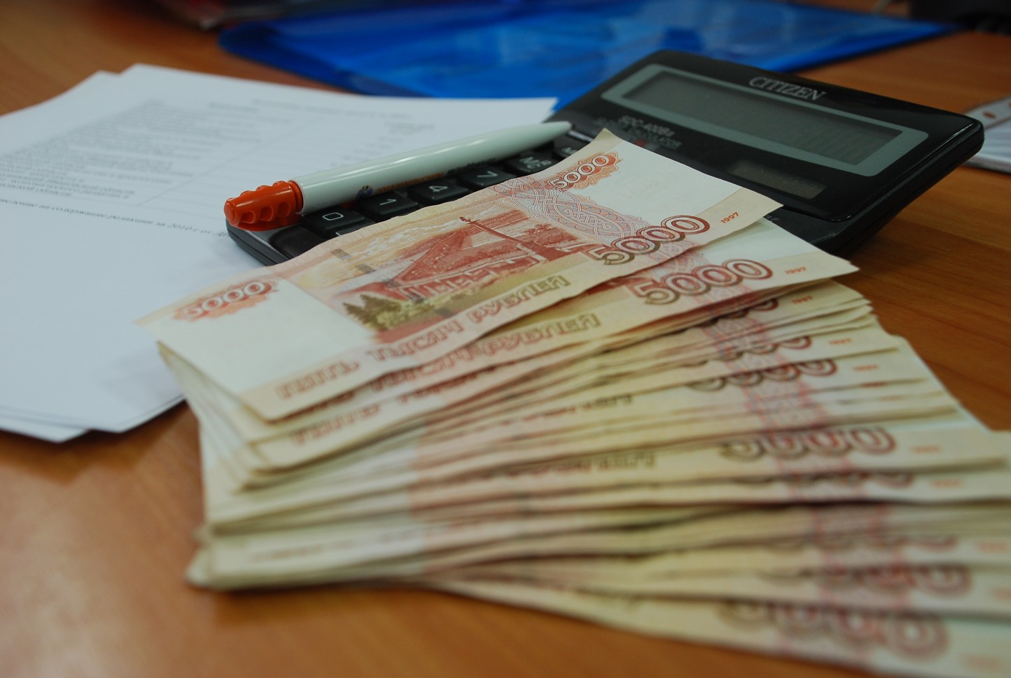 стопка банкнот по 5000 рублей на столе рядом с калькулятором, ручкой и документами