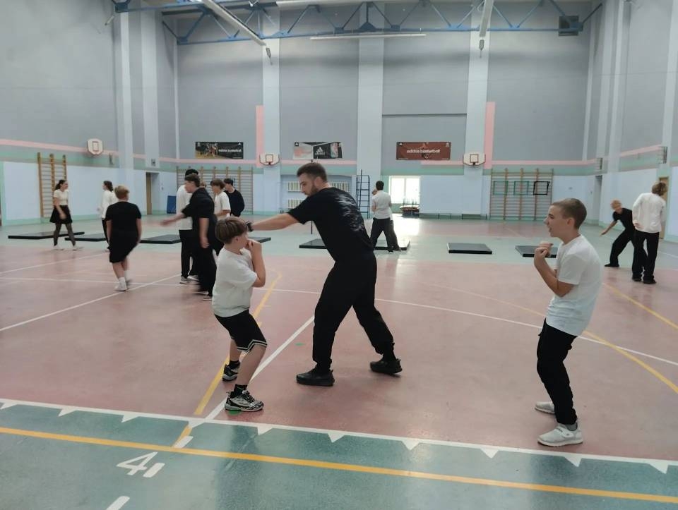 Тренировка в школьном спортзале: тренер показывает бойцовские приёмы нескольким школьникам