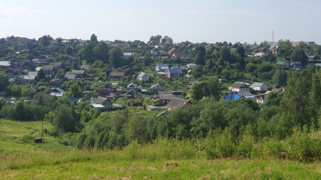 панорама сельской деревни с многочисленными деревянными домами и зелёными склонами